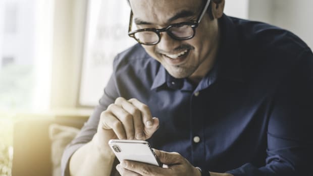 Person in glasses smiles while using their cell phone.